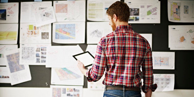 Businessman studying digital tablet in office conference room with project ideas on board rear view