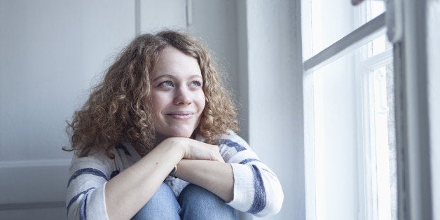 Germany, Bavaria, Munich, Young woman sitting at window, smiling