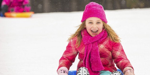 Happy girl expressing joy while sledding in the snow in winter.