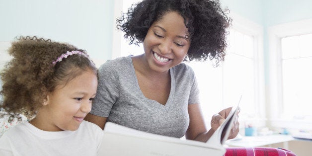 Happy mother and daughter reading book in bedroom