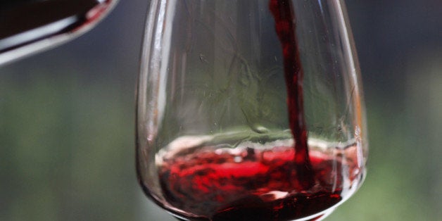 A woman pouring a sampling of red wine at a wine tasting, focus on hands