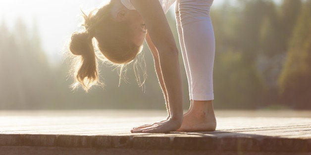 Young female sitting on dock practising yoga during sunrise/sunset.