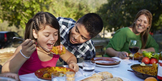 Girl trying to eat huge spoon of Paella with her brother at garden party