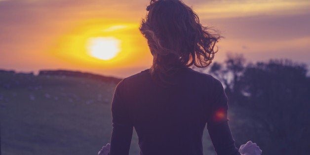 Rear view of young woman admiring the sunset over a field from her balcony