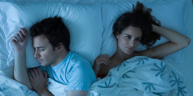 Couple lying together in bed, woman restlessly awake looking away