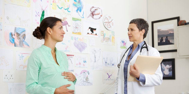 Doctor, aged 50, consulting with a pregnant woman, aged 25-30, in a medical center.