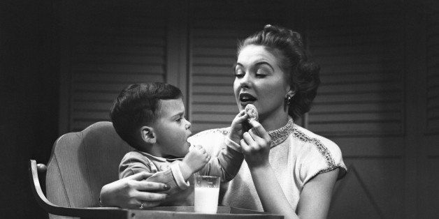Mother giving cookie to son (2-3) sitting in high chair, (B&W)