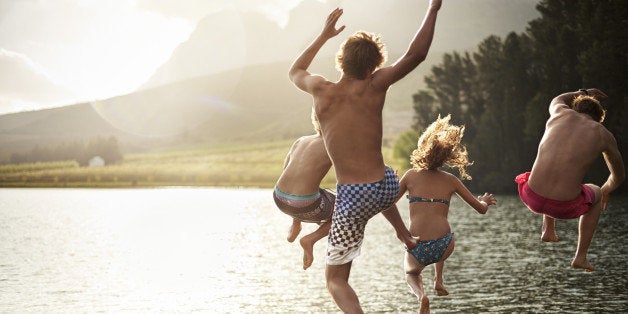 Four friends jumping into a lake with mountains in the background