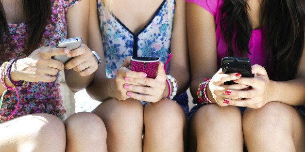 three girls chatting with their smartphones at the park