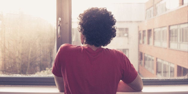 Young man is at the window silll and looking out at sunset