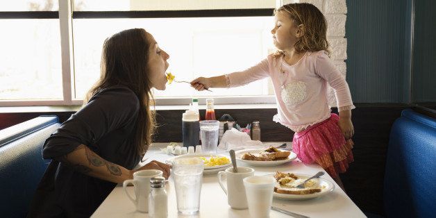 Toddler daughter feeding mother in diner