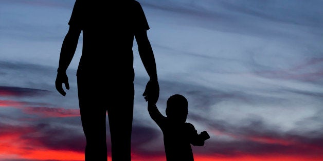 A royalty free image of a father and child holding hands and silhouetted against a sunset.