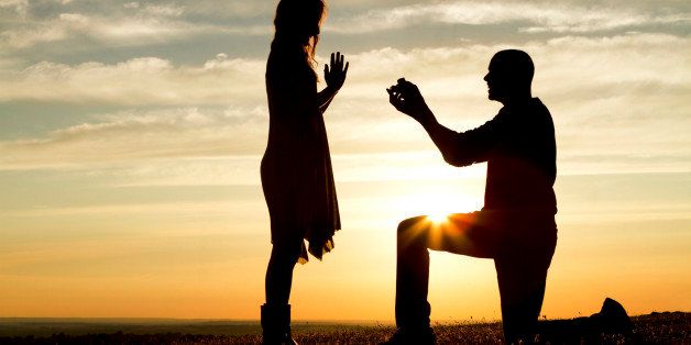 Silhouette of a man proposing marriage to a woman against the setting sun