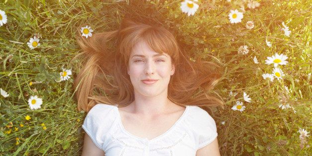 Woman laying in grass with daisies.
