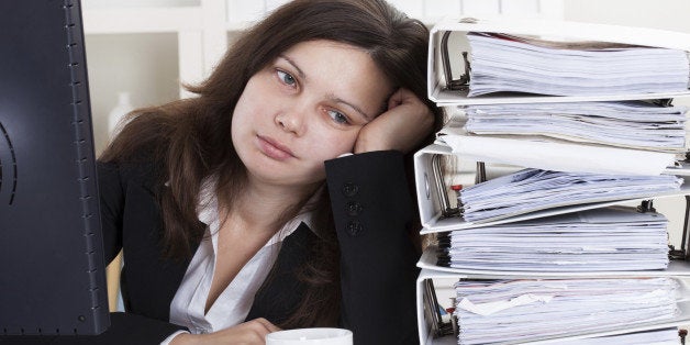 Stressed Businesswoman Working In Office With Stack Of Folders