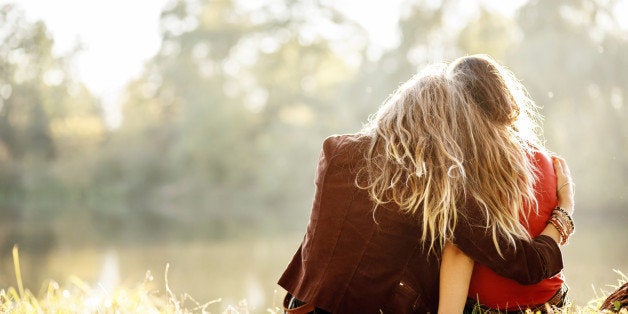 two young women sitting on grass hugging rear view