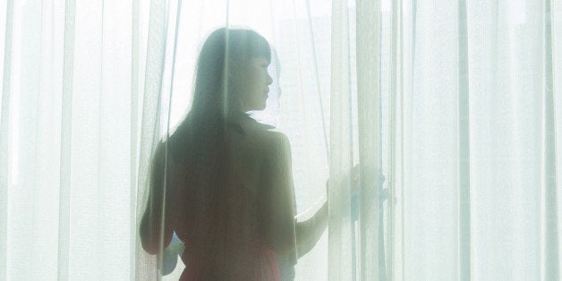 a woman in a red dress looking out of a sunlit window