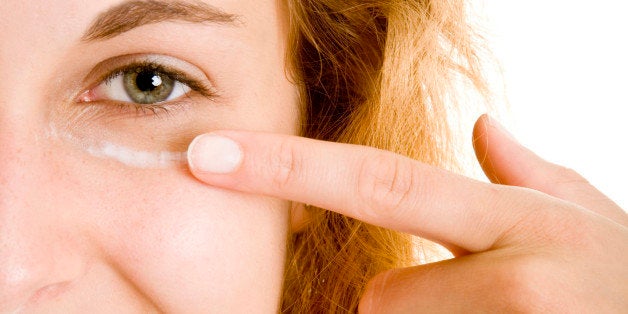 Young woman smiling and putting facial on the dark circle around her eye