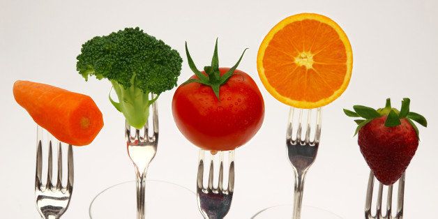 Five fresh fruits and vegetables, part of the daily recommended healthy diet, held on the prongs of forks, on a white background.