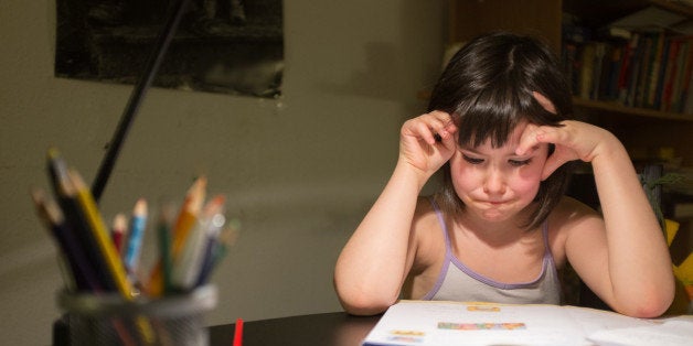 little girl at the table looking a little frustrated at her exercise book.