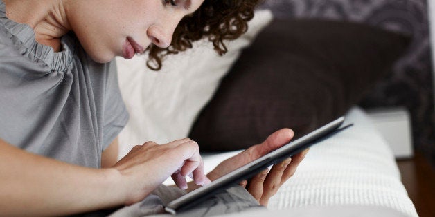 young woman lying in bed with tablet computer