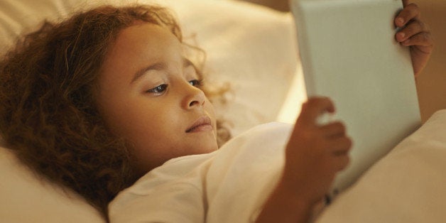 A young girl lying on her bed while using a digital tablet