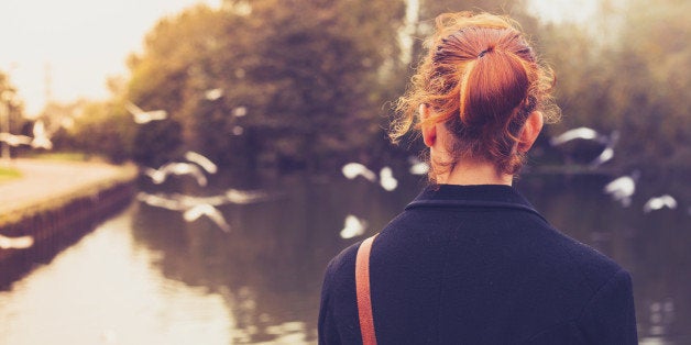 Rear view of a young redhead woman dressed in black looking at birds by a river