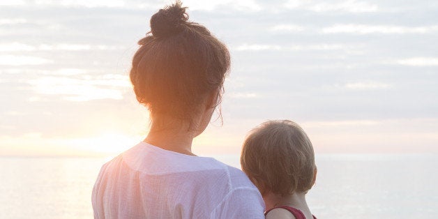 mother and baby son looking at sunrise at the beach in thailand