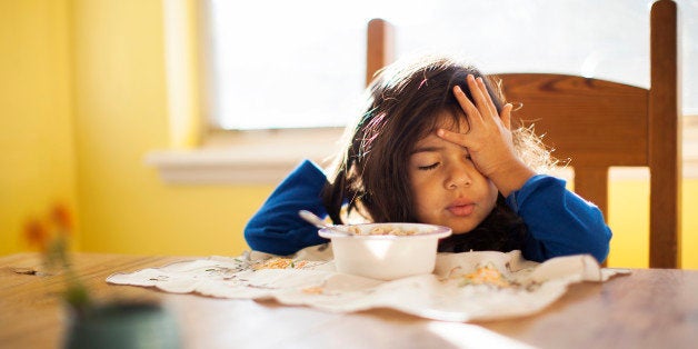 Tired toddler girl sitting at breakfast table.