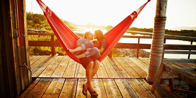 Husband and wife couple kissing in hammock on dock at sunset