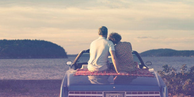 Couple sitting in convertible and embracing at sunset