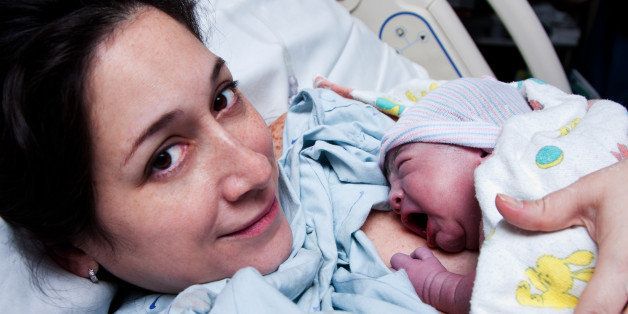 Beautiful new mother happy holding her infant baby after giving birth in hospital.