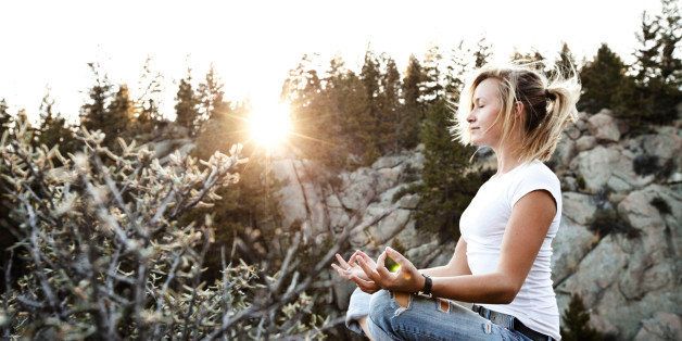 A beautiful young woman meditating on a cliff at sunset in Montana.