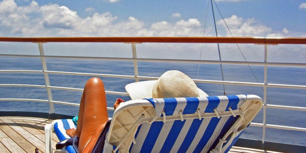 A woman sits on a lounge chair and overlooks the ocean from a cruise ship