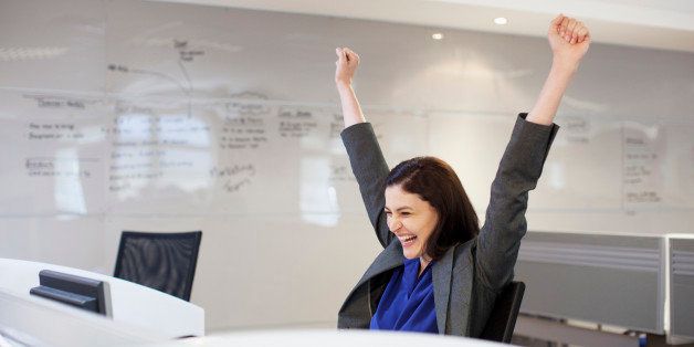 Enthusiastic businesswoman with arms raised in office