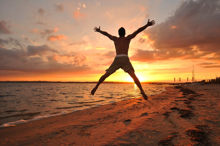 Young man jumping with spread arms celebrating and enjoying the moment at the seaside at sunset