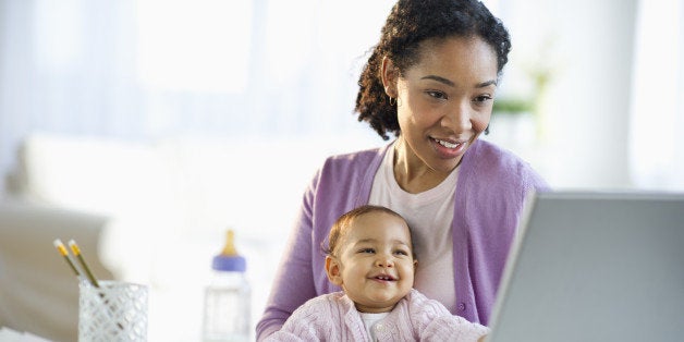 Mixed race woman holding baby and using laptop