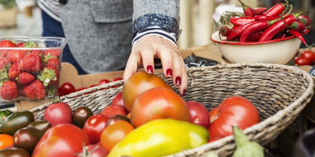 Close up of hand picking tomato from basket.