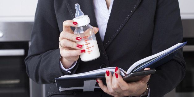 An elegant businesswoman working while holding her child's milk bottle