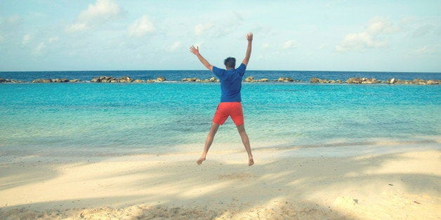 Happy young man jumping in the air at sea on white snd beach