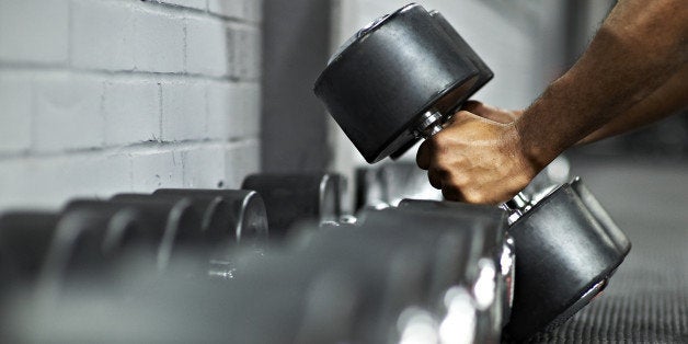 Strong black male picking up dumbbells from selection of free weights in gym, ready for workout