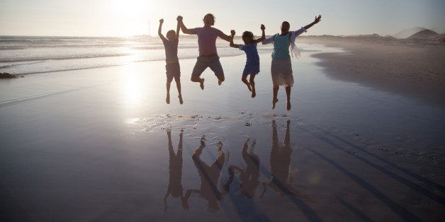 Family with two children jumping together on a beach at sunset