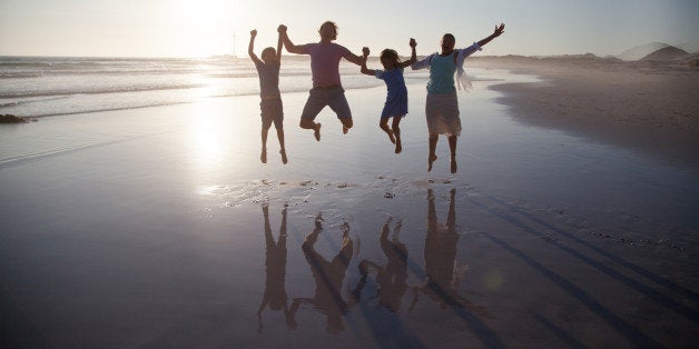 Family with two children jumping together on a beach at sunset