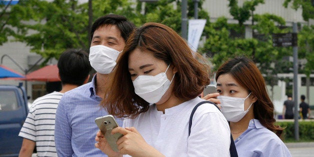 A woman wears a mask as a precaution against Middle East Respiratory Syndrome (MERS) virus as she uses her smartphone on a street in Seoul, South Korea, Tuesday, June 2, 2015. South Korea on Tuesday confirmed the country's first two deaths from MERS as it fights to contain the spread of the virus that has killed hundreds of people in the Middle East. (AP Photo/Ahn Young-joon)