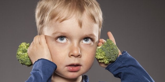 Portrait of little boy holding broccoli on his ears