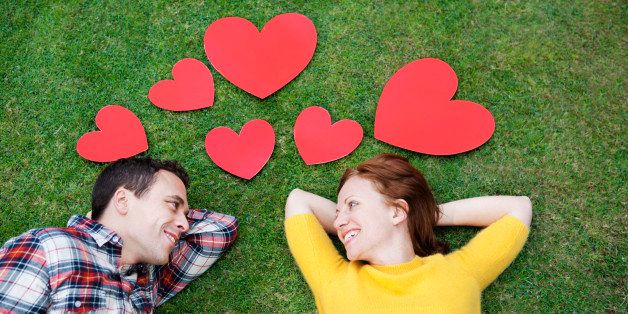 Couple laying in grass,surrounded by hearts.