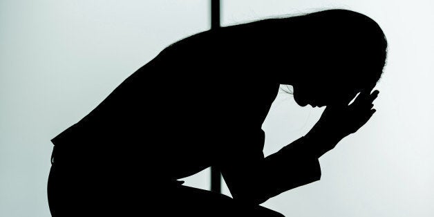 Silhouette of depressed young businesswoman in formalwear holding head in hands while sitting on her suitcase in airport