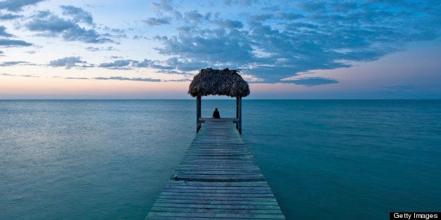 This is an image of a beautiful sunset in the Carribean taken from a dock on the beach with a palm thatched roof.