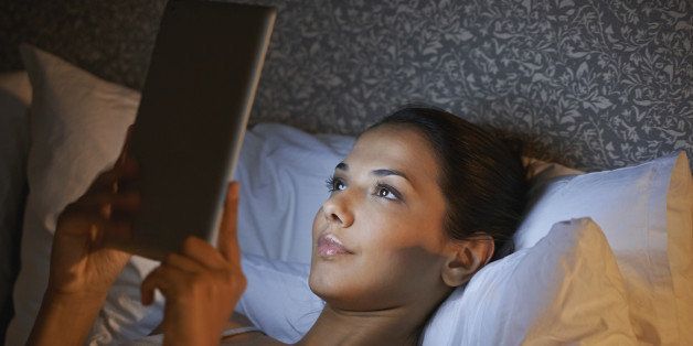Beautiful young woman playing on her digital tablet before bed