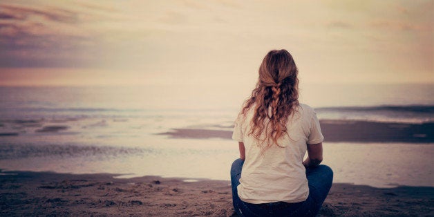 Lady sitting by sea edge in the evening looking at the sea.